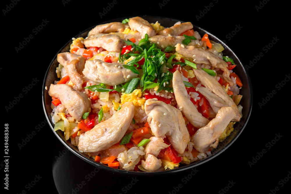 A plate of delicious rice with chicken in sauce and vegetables: carrots, sweet peppers, greens, spices on a black background A plate of delicious rice with chicken in sauce and vegetables: carrots, sweet peppers, greens, spices on a black background