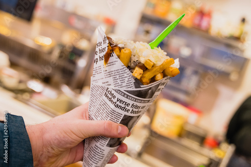 Human hand holding golden french fries wrapped in a newspaper with fresh onions