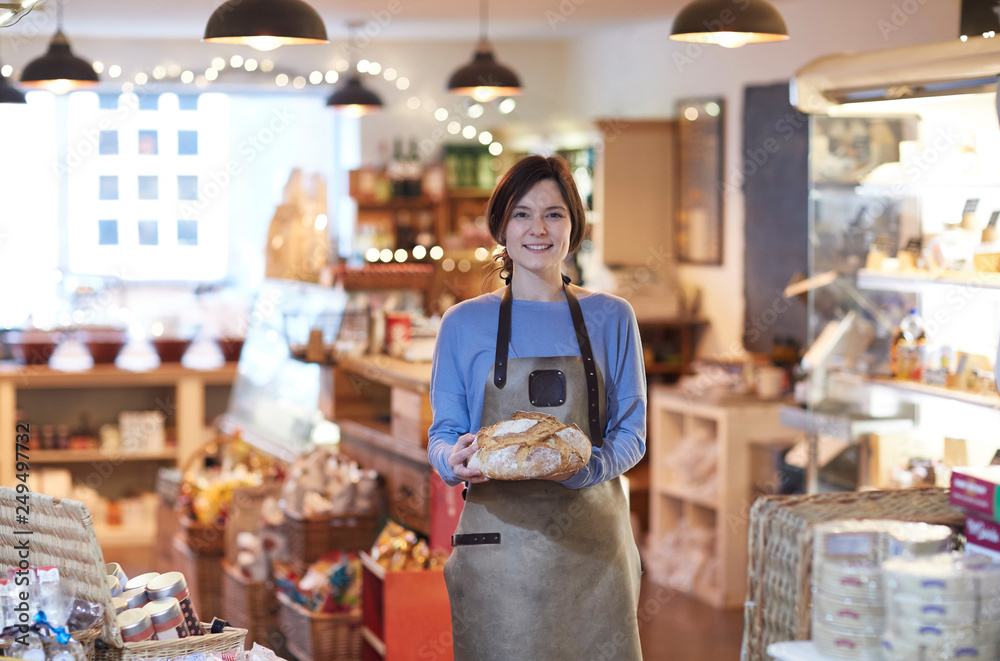 Φωτογραφία Portrait Of Smiling Female Owner Of Delicatessen Shop Wearing Apron Holding Loaf
