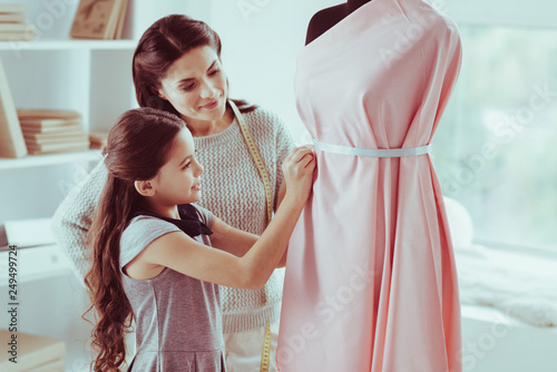 Waist up of pleasant girl assisting her mother with dress sewing