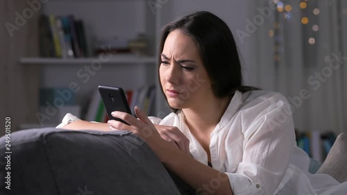 Sad lady checking smart phone content sitting on a couch in the night at home