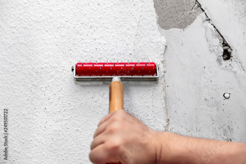 Alte Rauhfasertapete wird mit einer Stachelwalze oder Nagelwalze präpariert  um sie anschließend mit Spülmittel aufzuweichen. Danach wird die Tapete  entfernt Stock Photo | Adobe Stock