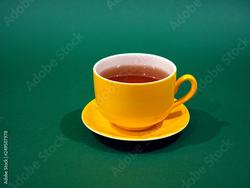Yellow cup with tea and lemon on a green background