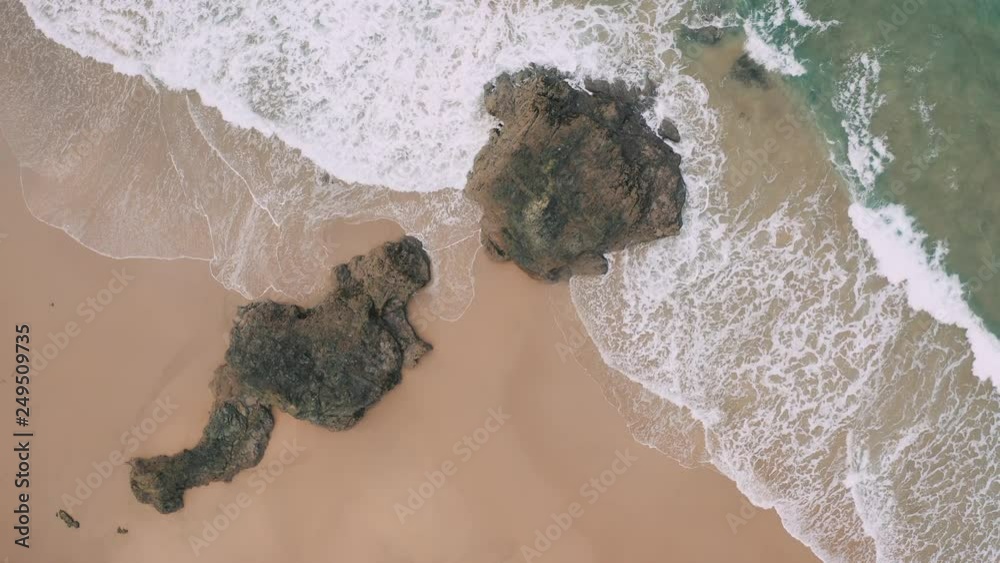 Aerial top down view of wide beautiful beach with big waves and surfers;drone flight over the sandy beach; giant rocks in the middle of the beach; camera moves away; Aerial top down view of wide beautiful beach with big waves and surfers;drone flight over the sandy beach; giant rocks in the middle of the beach; camera moves away;