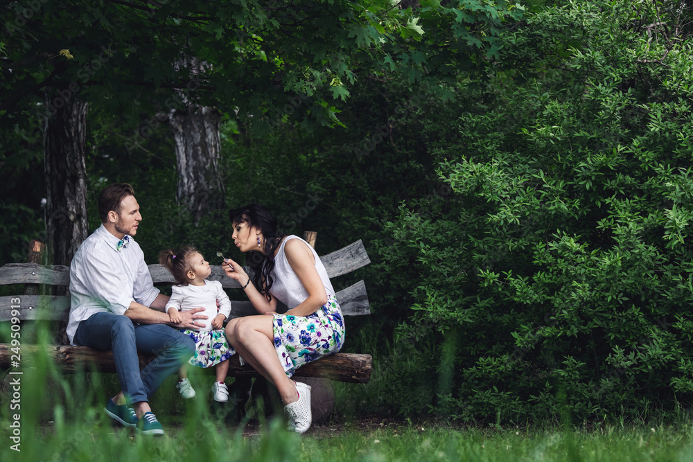 friendly happy family resting on a wooden bench and playing with a dandelion friendly happy family resting on a wooden bench and playing with a dandelion