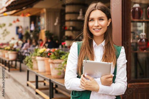Beautiful brunette business woman in white blouse and green jacket working on a tablet in her hands outdoors. Freelancer in european city. Space for text