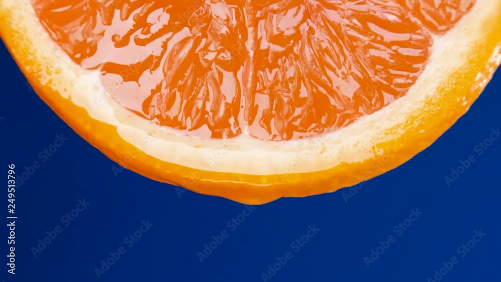 sliced orange fruit with drops of juice falling from it in slow motion. Closeup macro shot. Fresh berry and fruit series.