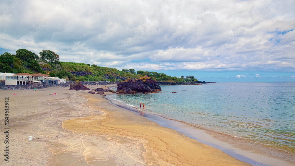 Fototapeta premium Sandy beach with black volcanic rocks at coast near the Vila Franca do Campo town, located on Sao Miguel island of Azores, Portugal.