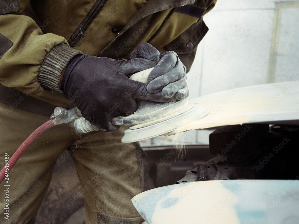 men's hands in black gloves polish the hood of the car with a pneumatic polisher in the garage