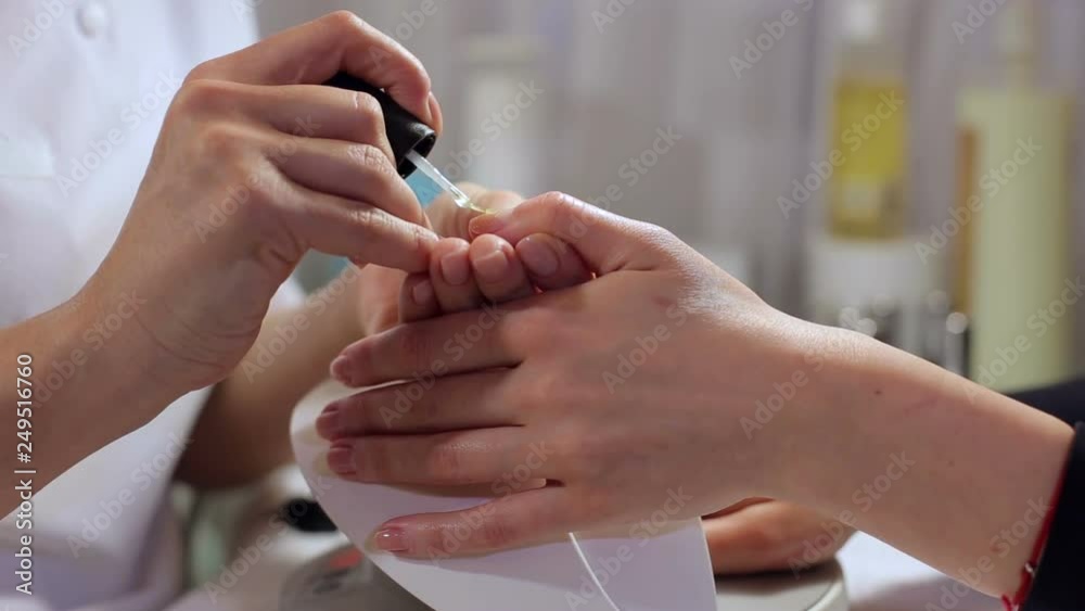 Close-up of manicurist painting nails with transparent nail polish to a young girl in a beauty salon. Manicurist master makes manicure on young woman hand. Close-up of manicurist painting nails with transparent nail polish to a young girl in a beauty salon. Manicurist master makes manicure on young woman hand.