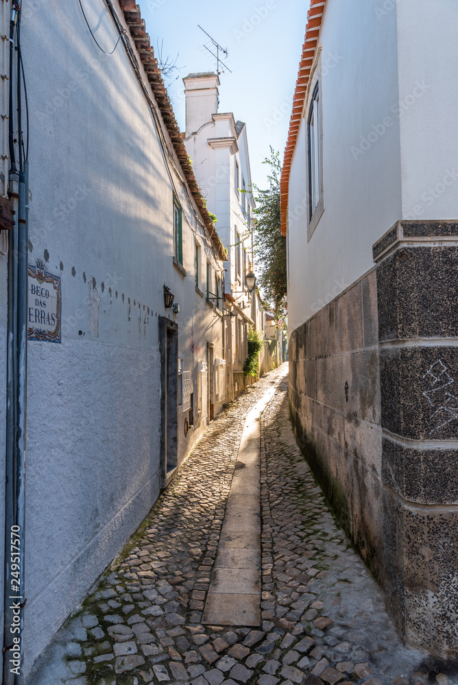 Narrow cobblestone alley between whitewashed houses in Cascais, Portugal
