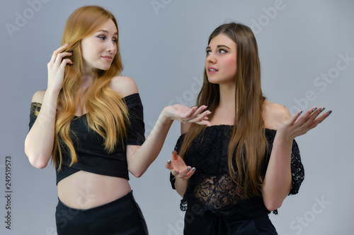 A concept portrait of two cute beautiful girls talking on a gray background in the studio