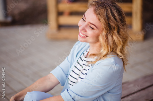 Joyful and cheerful woman in blue wearing and striped t-shirt. Long curly light hair. Wearing stylish blue jacket. Joyful and cheerful woman smiling to camera.
