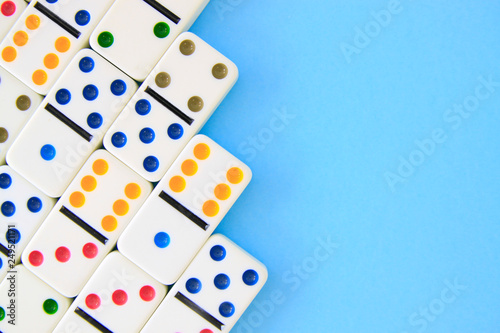 White dominoes with brightly colored dots on blue background shot overhead with copy space