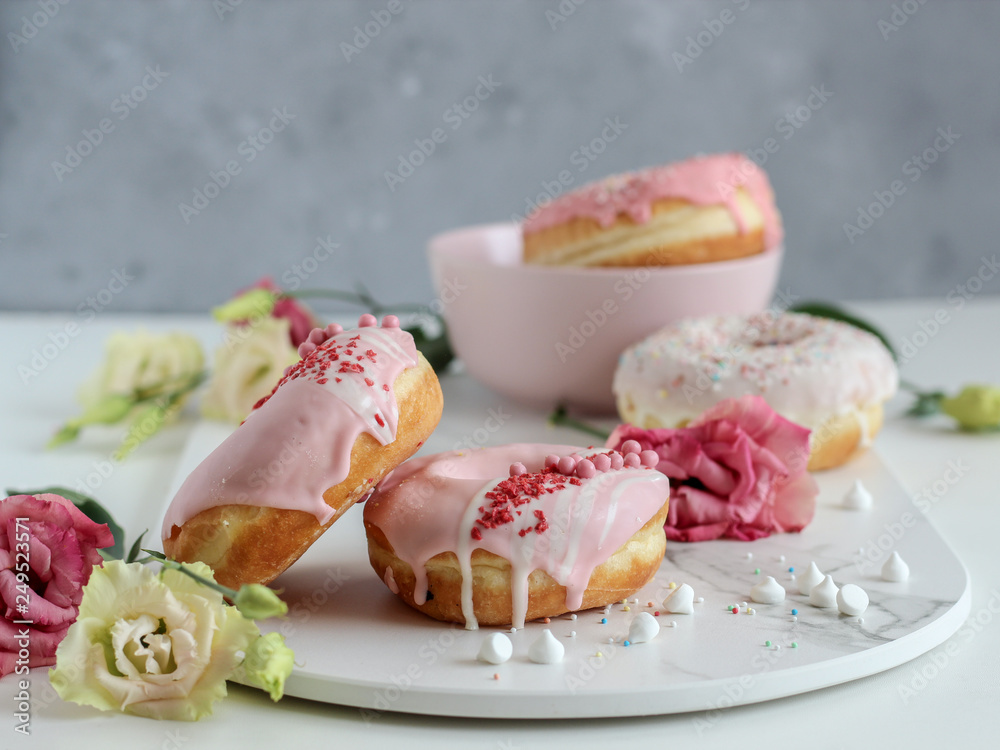 A stack of pink donuts with flowers on a dark background A stack of pink donuts with flowers on a dark background