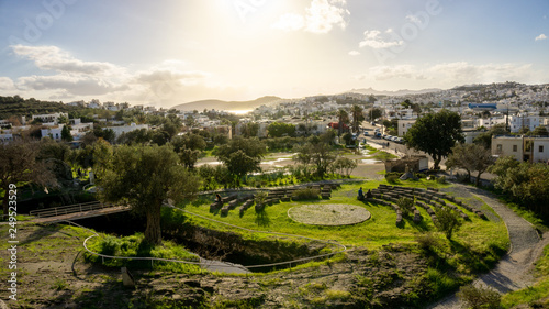 Myndos gate view of a bay of Bodrum, Mugla, Turkey. Beautiful sunset over the white houses and the archaeological ruins of the old city wall. Olive and palm trees