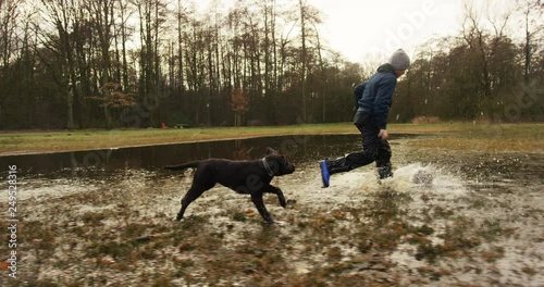 Happy boy and wild puppy playing in deep puddle of mud in autumnal park