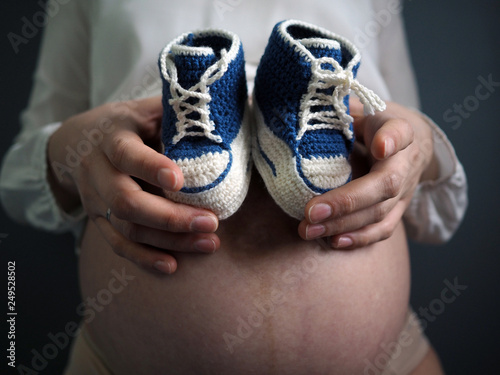 Pregnant woman holding small baby shoes relaxing at home