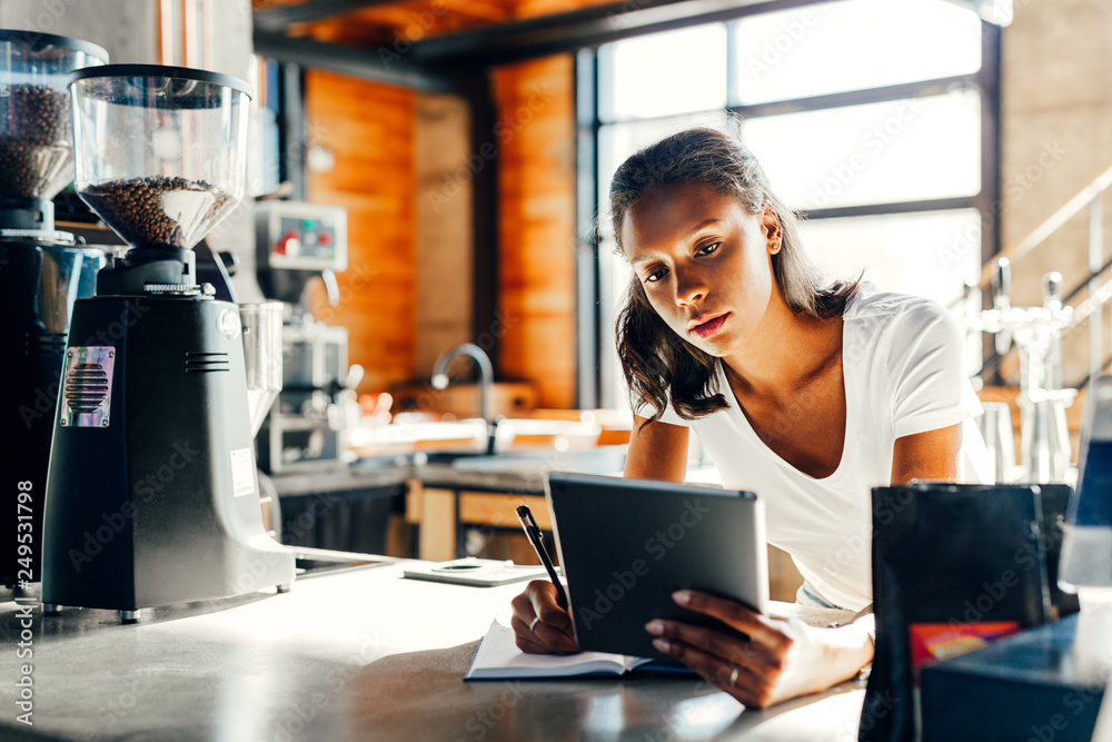 Cafe owner leaning on counter making notes in cafe Cafe owner leaning on counter making notes in cafe