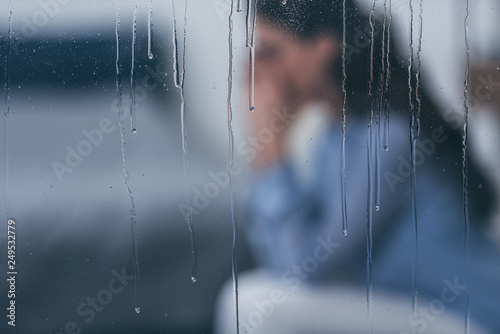 Fotografie, Obraz selective focus of raindrops on windows with sad woman sitting on background