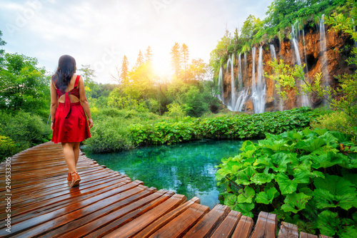 Woman traveler walking on wooden path trail with lakes and waterfall landscape in Plitvice Lakes National Park, UNESCO natural world heritage and famous travel destination of Croatia. photo