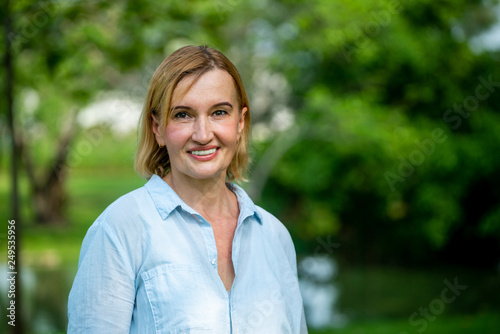 Portrait of happy middle aged woman standing in the park. The woman is smiling with happiness. photo