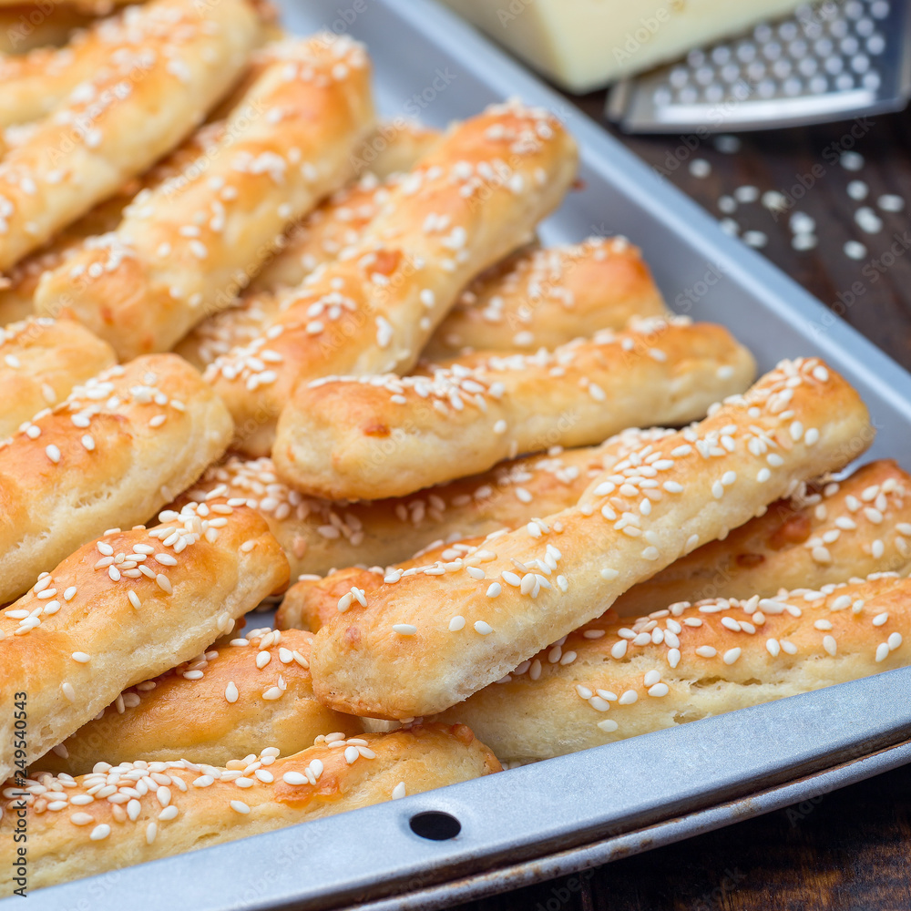 Homemade savory bread sticks with cheese and sesame on baking tray, square format