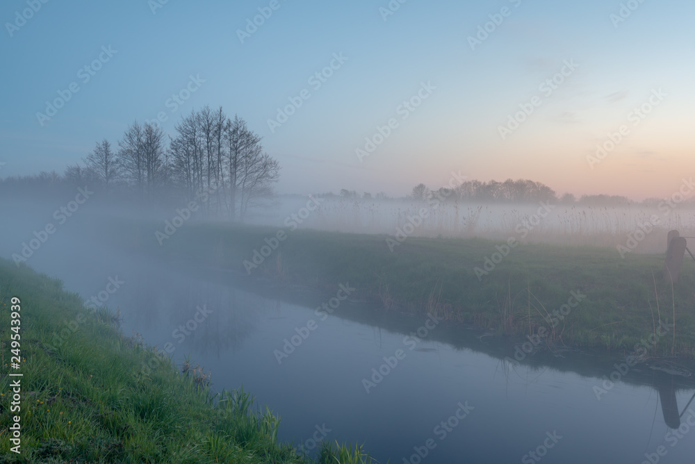 Mysterious foggy evening in a field near the river at the sunset time. Karwia village in Poland.