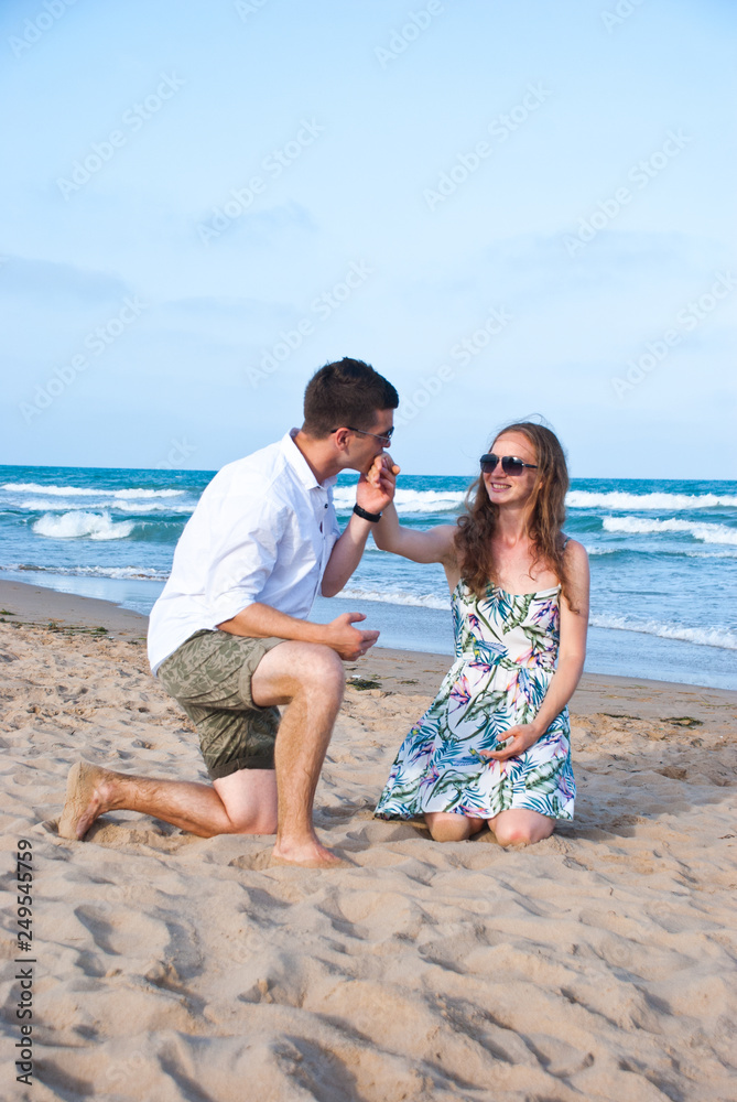 Loving couple on sea sandy beach - a man making decloration of love. Happy family spend their vacation on th sea.