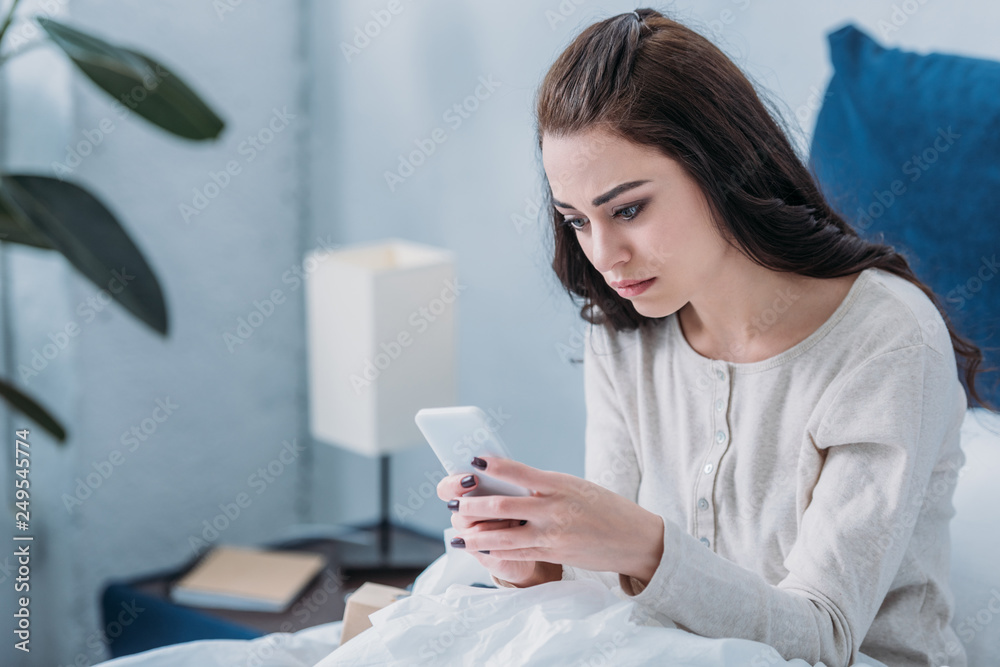 selective focus of depressed woman lying in bed and using smartphone selective focus of depressed woman lying in bed and using smartphone