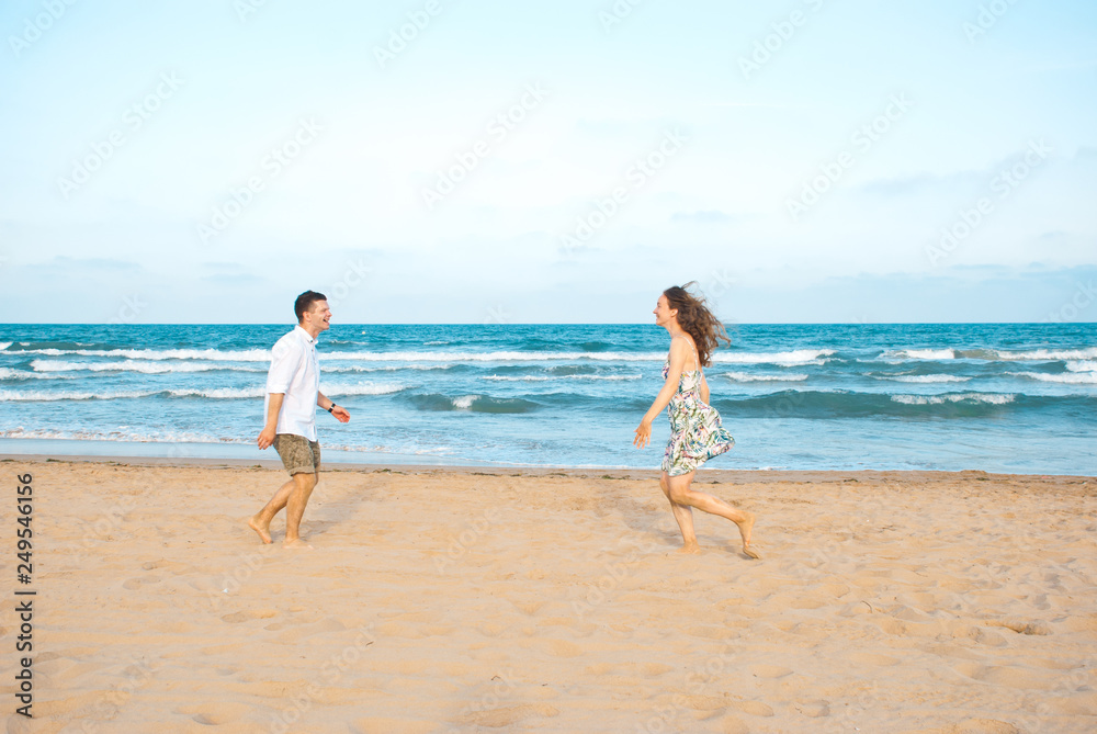 Euphoric young couple running to each other on the sea beach. Horizontal shape, side view, copy space. Happy moment for lovers.