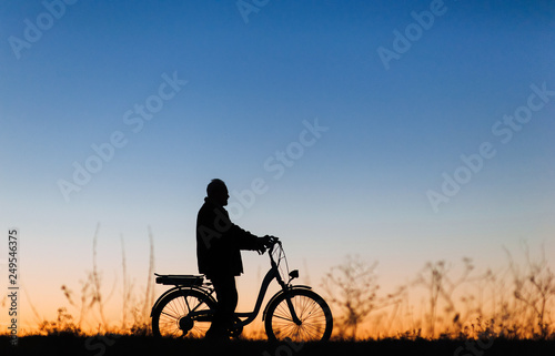 Active pension. Male cyclist on the e-bike or electric bicycle on the sunset background. Silhouette of the old man in profile. Travel. Sport.