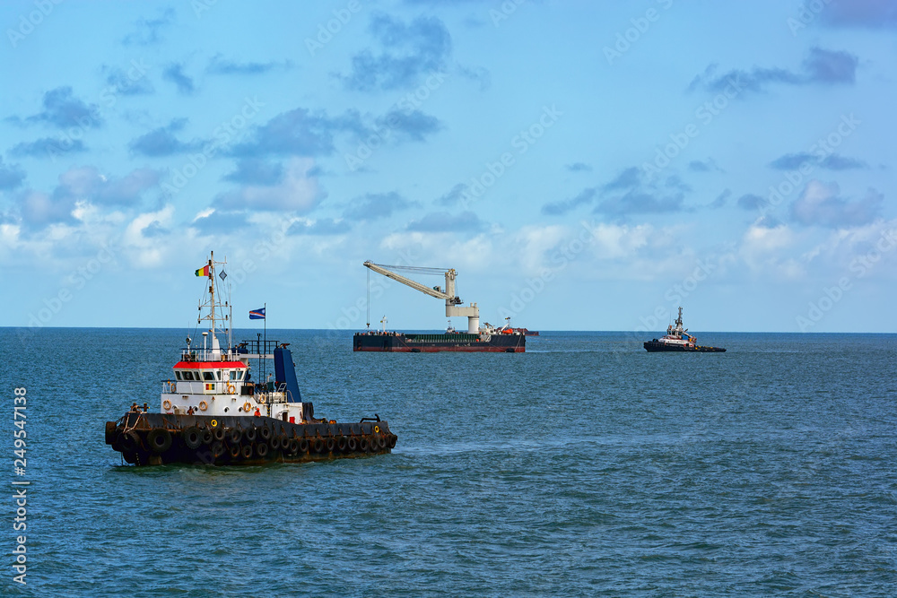 Tugboats assists Floating Crane Transhipper in Bauxite transshipment operations at anchorage off Port Kamsar, Republic of Guinea.