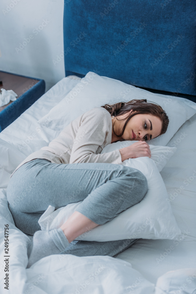 sad woman in pajamas holding pillow and lying in bed at home sad woman in pajamas holding pillow and lying in bed at home