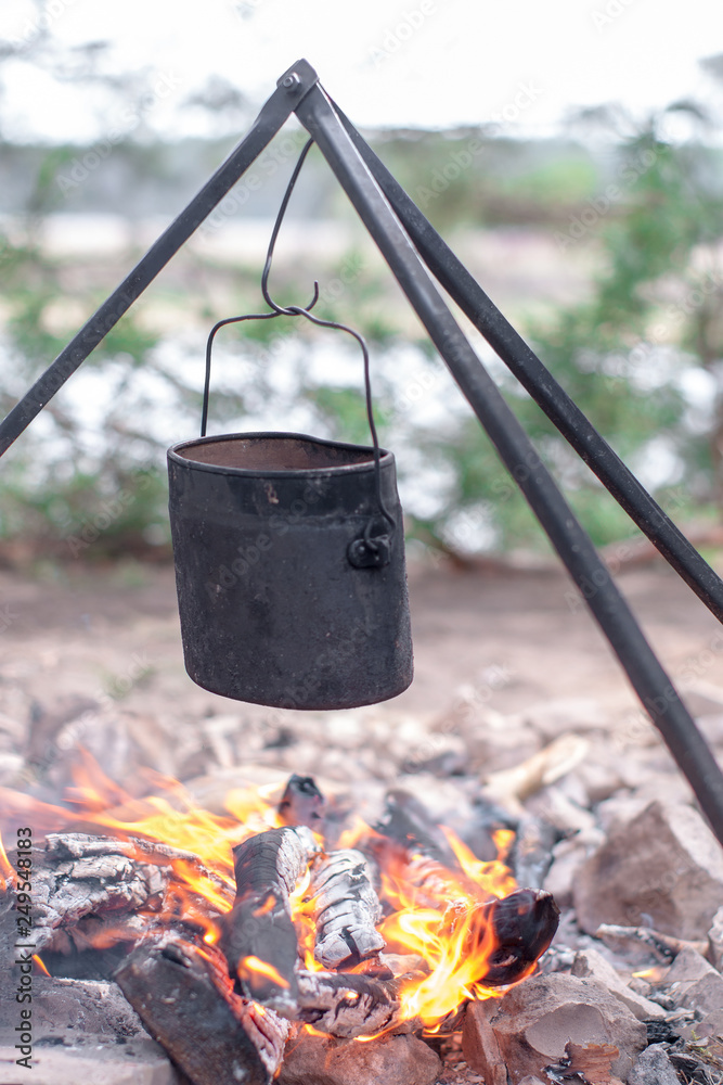 Tourist pot hanging over campfire tripod on background of river Tourist pot hanging over campfire tripod on background of river