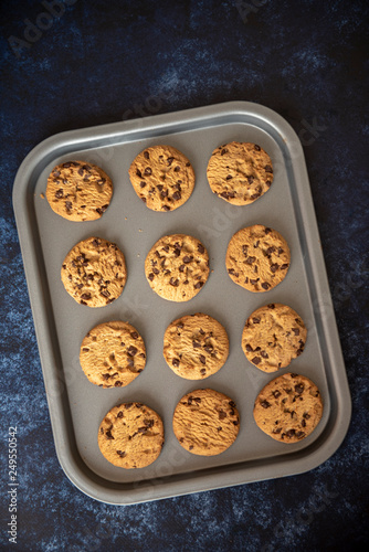 Vertical image of chocolate chip cookies on a baking tray, taken on a dark blue background