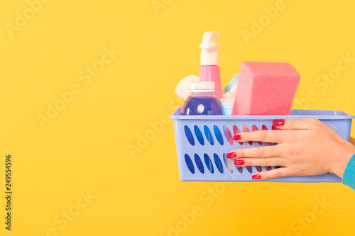 Cleaning products shopping. Basket of supplies in woman hands. Copy space on yellow background.