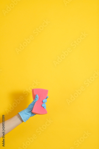 Cleaning concept. Hand in rubber glove holding sponge. Copy space on yellow background.