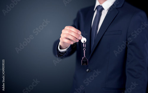 Young businessman hand over keys with empty dark background 