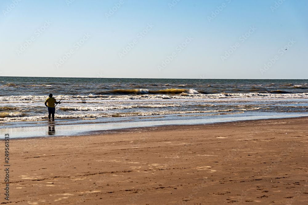 Silhouette of a man fishing alone on the beach with a view of the horizon