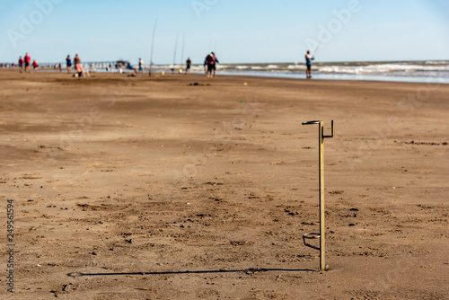 Selective focus on golden fishing rod holders nailed in sand with view of the coast and fishermen behind