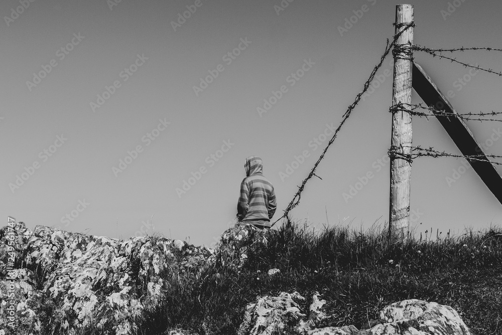 Obraz premium Black & white image of one man in a field next to a barbed wire fence with a cloudless sky.
