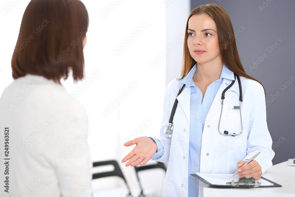 Doctor and patient discussing something while standing near reception desk in emergency hospital. Physician at work in clinic. Medicine and health care concept Doctor and patient discussing something while standing near reception desk in emergency hospital. Physician at work in clinic. Medicine and health care concept