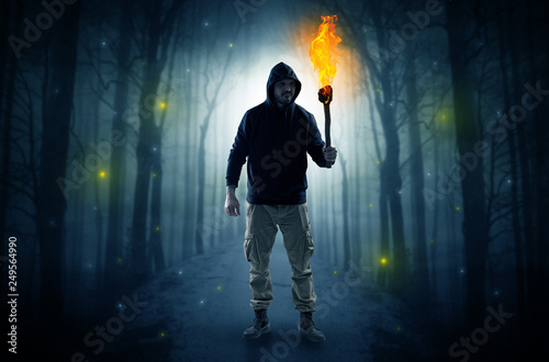 Mysterious man coming from a path in the forest with burning flambeau concept 