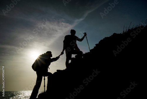 The joint work teamwork of two people man and girl travelers help each other on top of a mountain climbing team, a beautiful sunset landscape.