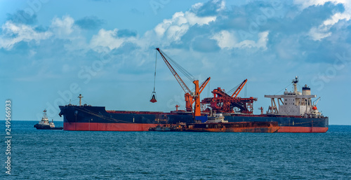 Loading ocean-going bulk carrier ship with Bauxite aluminum ore from the mini bulk carrier (feeder) vessel at offshore Kamsar port, Guinea, West Africa.