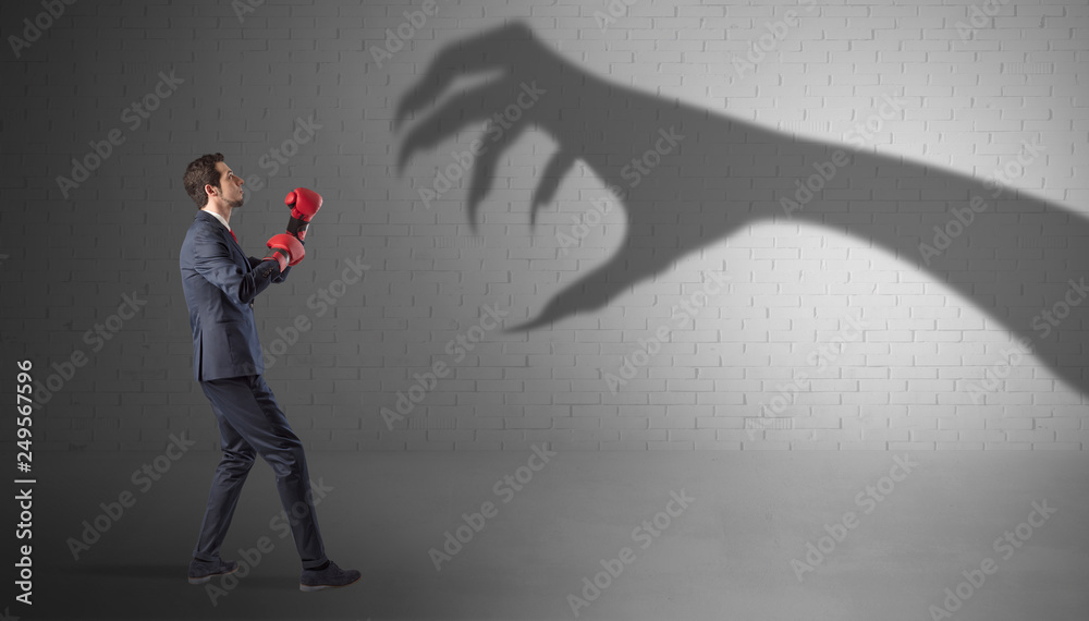 Fototapeta premium Tiny businessman fighting with scary hand shadow 