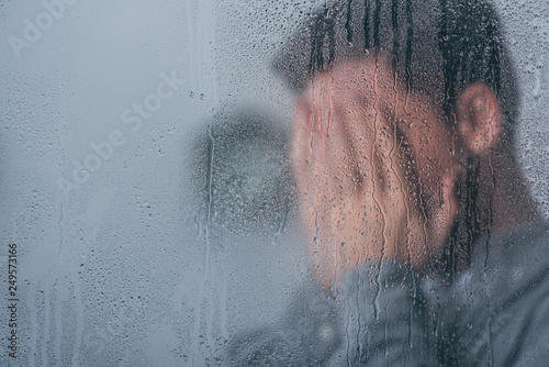 Murais de parede selective focus of raindrops on window with man covering face and crying on back