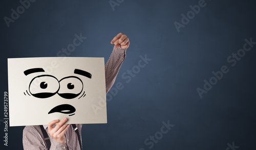 Casual person holding a paper with funny emoticon in front of her face
