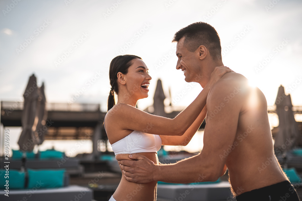 Waist up of excited couple hugging on the beach and smiling